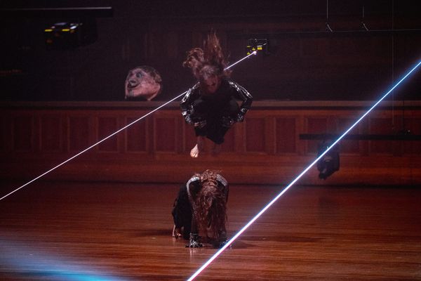 One dancer leaps above another crouched on the timber floor as blue-white laser beams slice across Melbourne Town Hall in Chunky Move’s Time Remaining.
