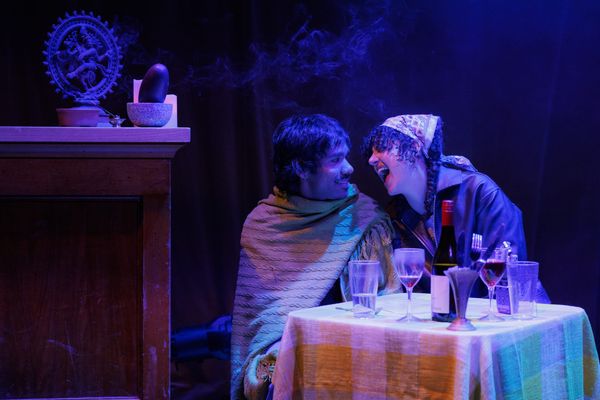 Jamie and Zahra sit together at a dining table under purple stage lighting in Cut Chilli.