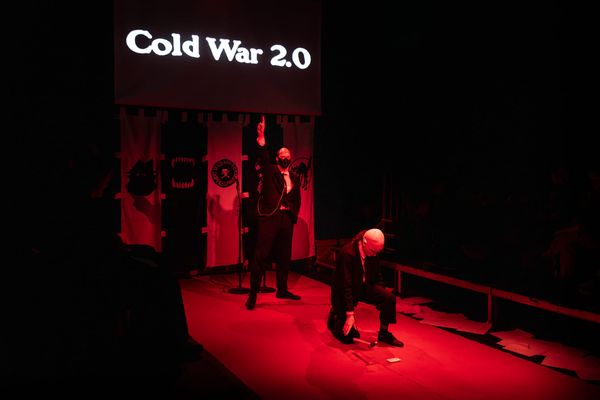 Tobias Manderson-Galvin and Aquilla Sorensen perform on a sparsely furnished stage washed in red light in Cold War 2.0.