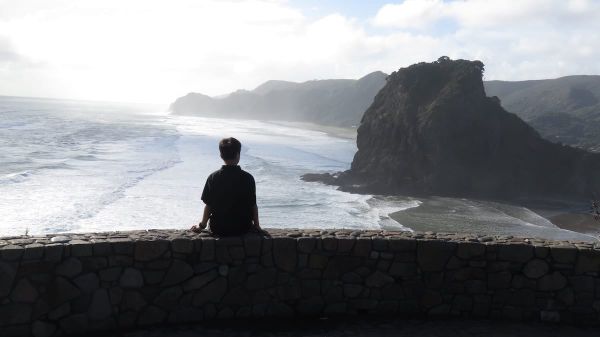 boy sits on a wall at stares out at the ocean