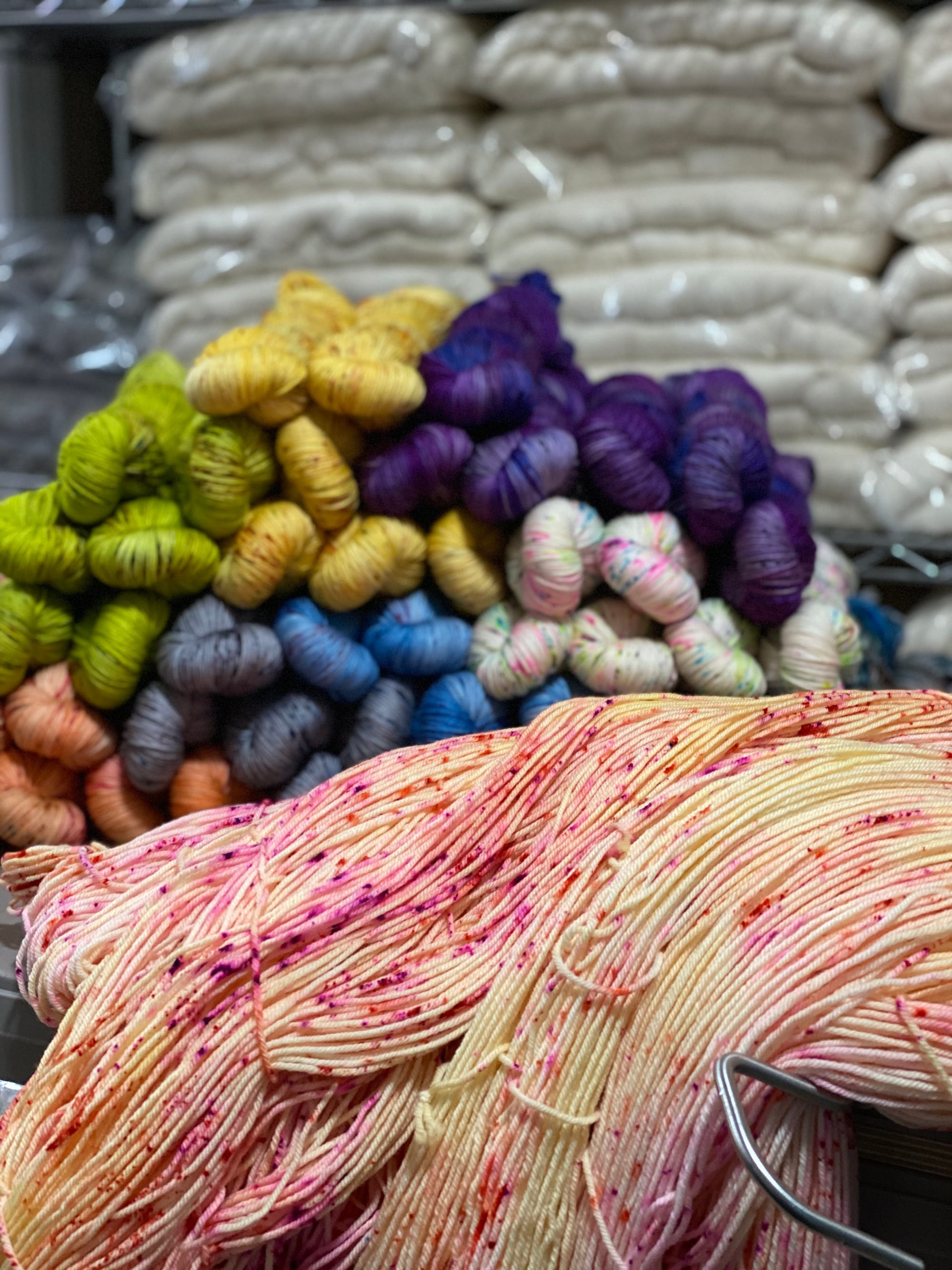 Colorful yarn skeins stacked in a shelving unit, featuring various vibrant colors with speckled yarn in the foreground.