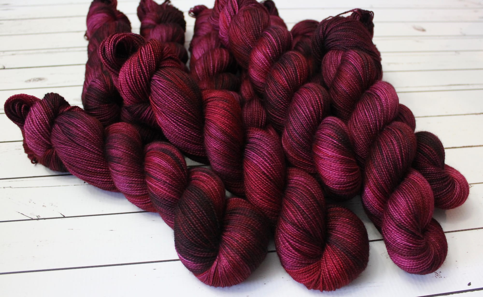 Pile of deep burgundy yarn skeins on a white wooden surface.