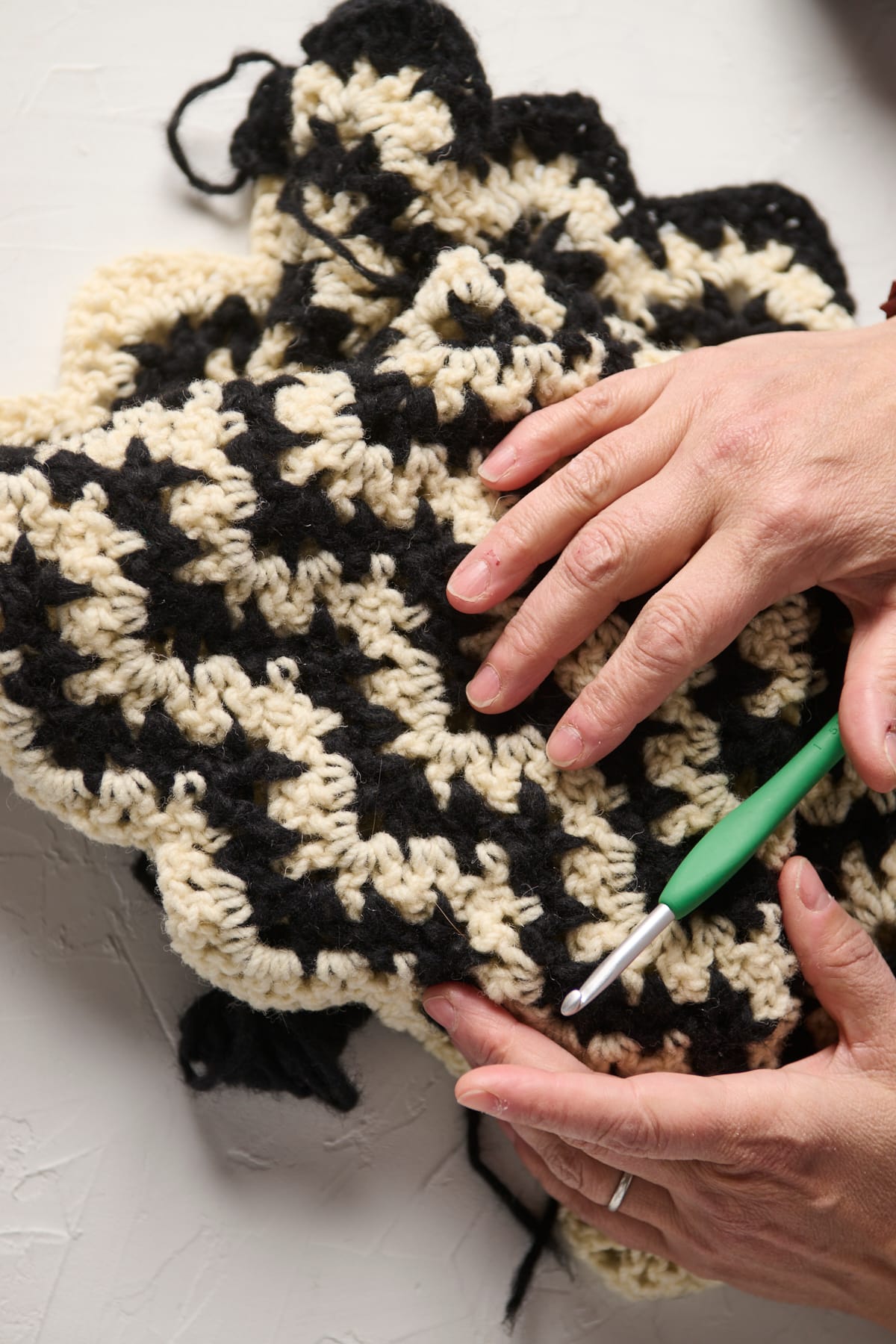 Close-up of hands and a green crochet hook on a black and white crocheted blanket.