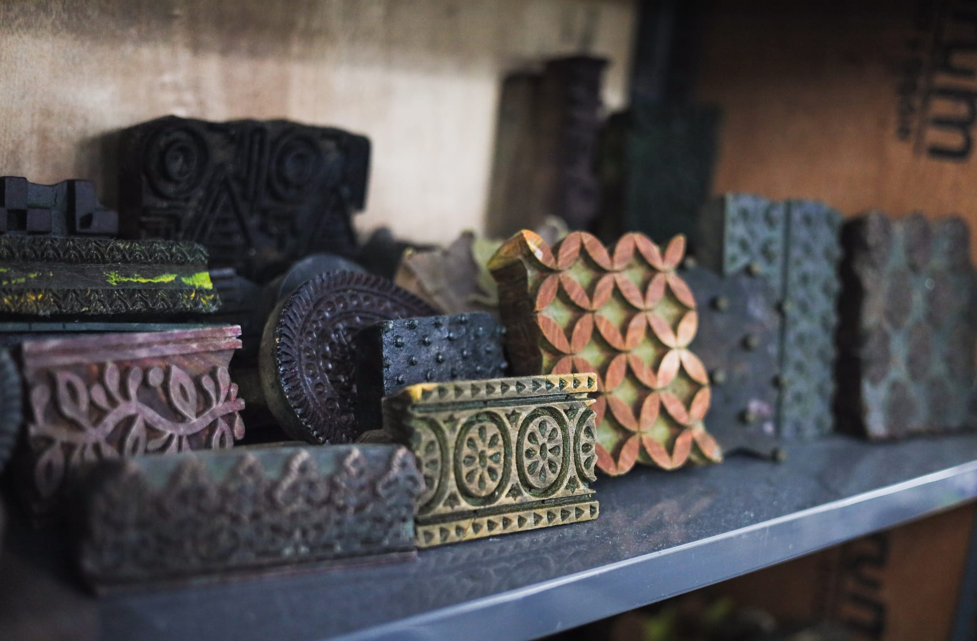A collection of intricately carved wooden textile printing blocks on a shelf, featuring diverse patterns and textures. The scene conveys creativity and craftsmanship.
