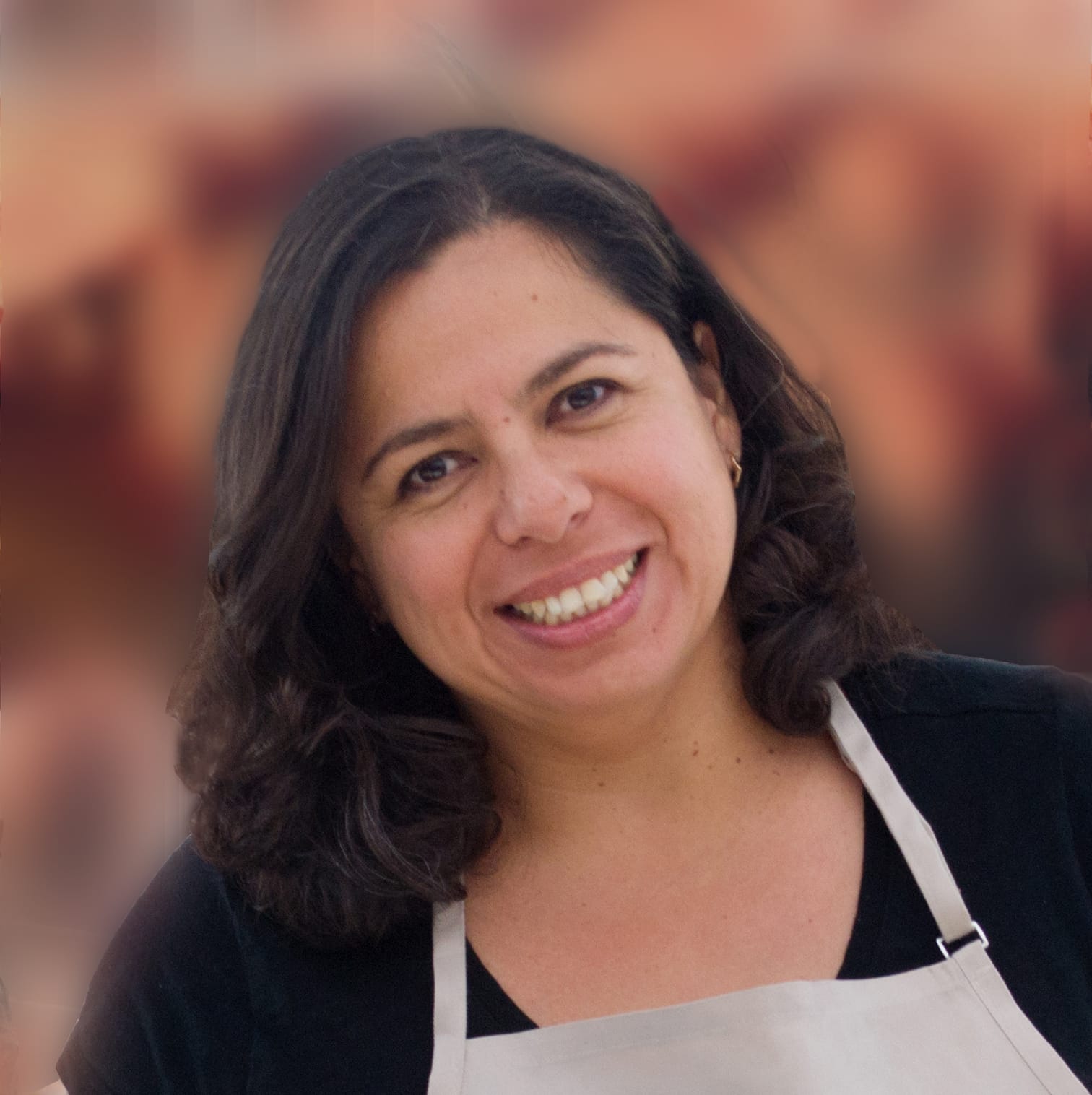 Portrait of a woman smiling. She has dark hair and is wearing a black shirt and white apron. The woman is MariAngeles Davila.
