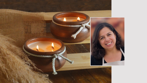 Two round clay candle holders with flickering candles on a wooden surface, with a smiling woman in an apron on the right.
