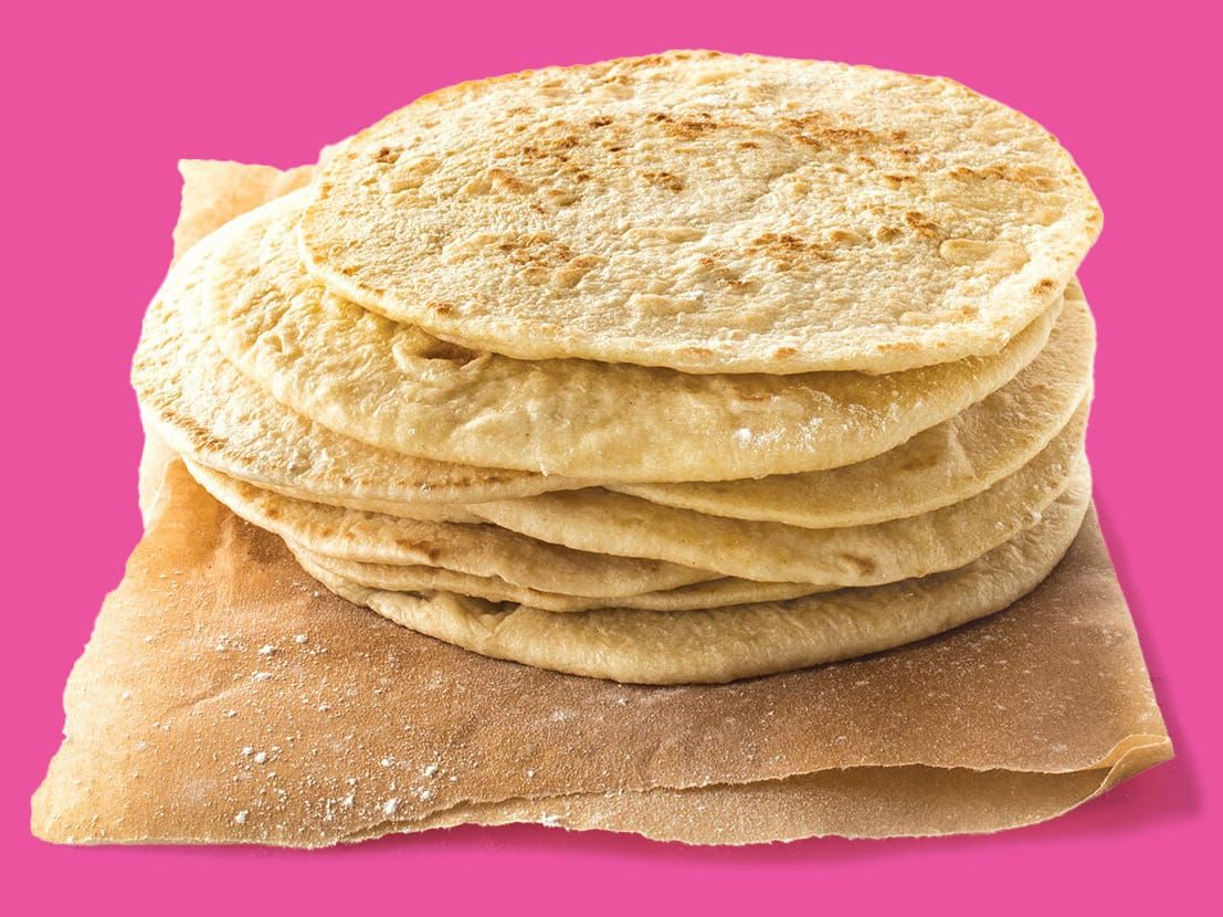 A stack of Taco Cabana flour tortillas sitting on parchment paper with a pink background.