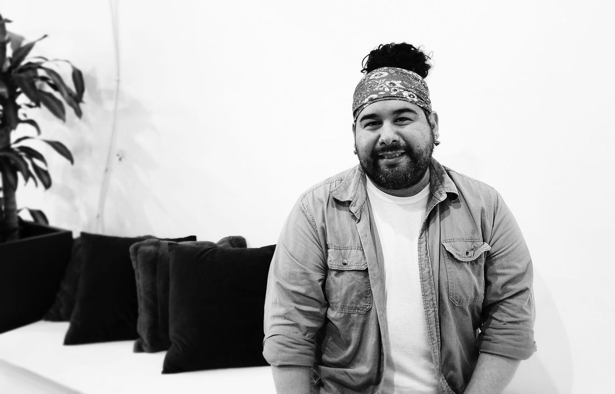 A person wearing a jacket sitting on a couch, with pillows behind them.