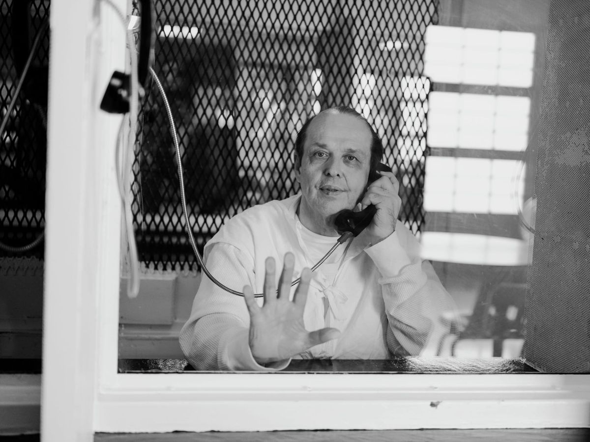 A man in prison with his hand against the glass while holding a phone