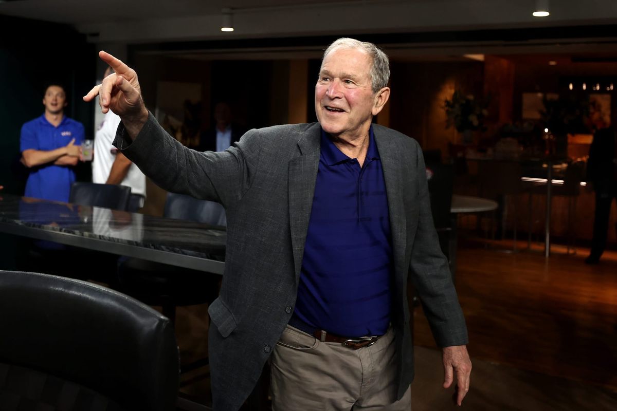 George W. Bush pointing off screen, wearing a navy shirt and a gray blazer