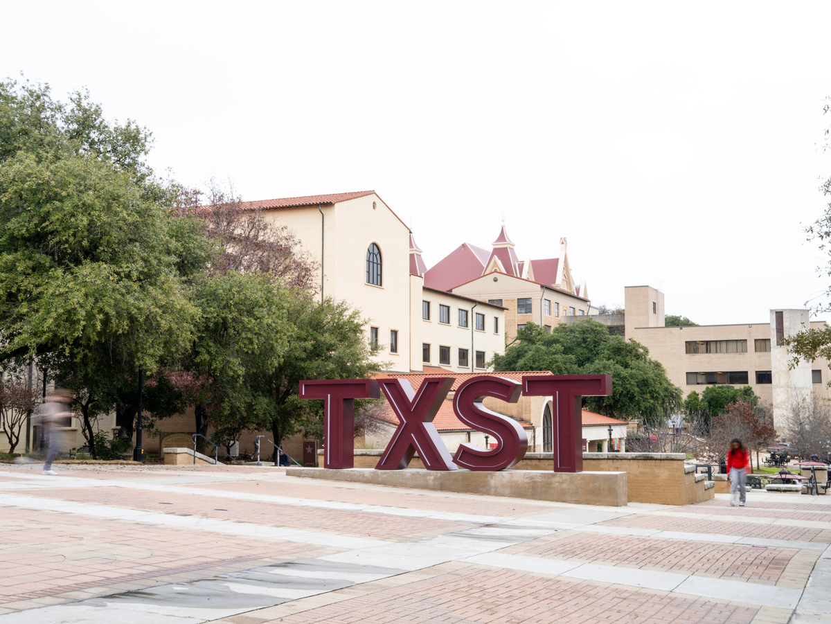 the texas state sign on campus with a student walking by
