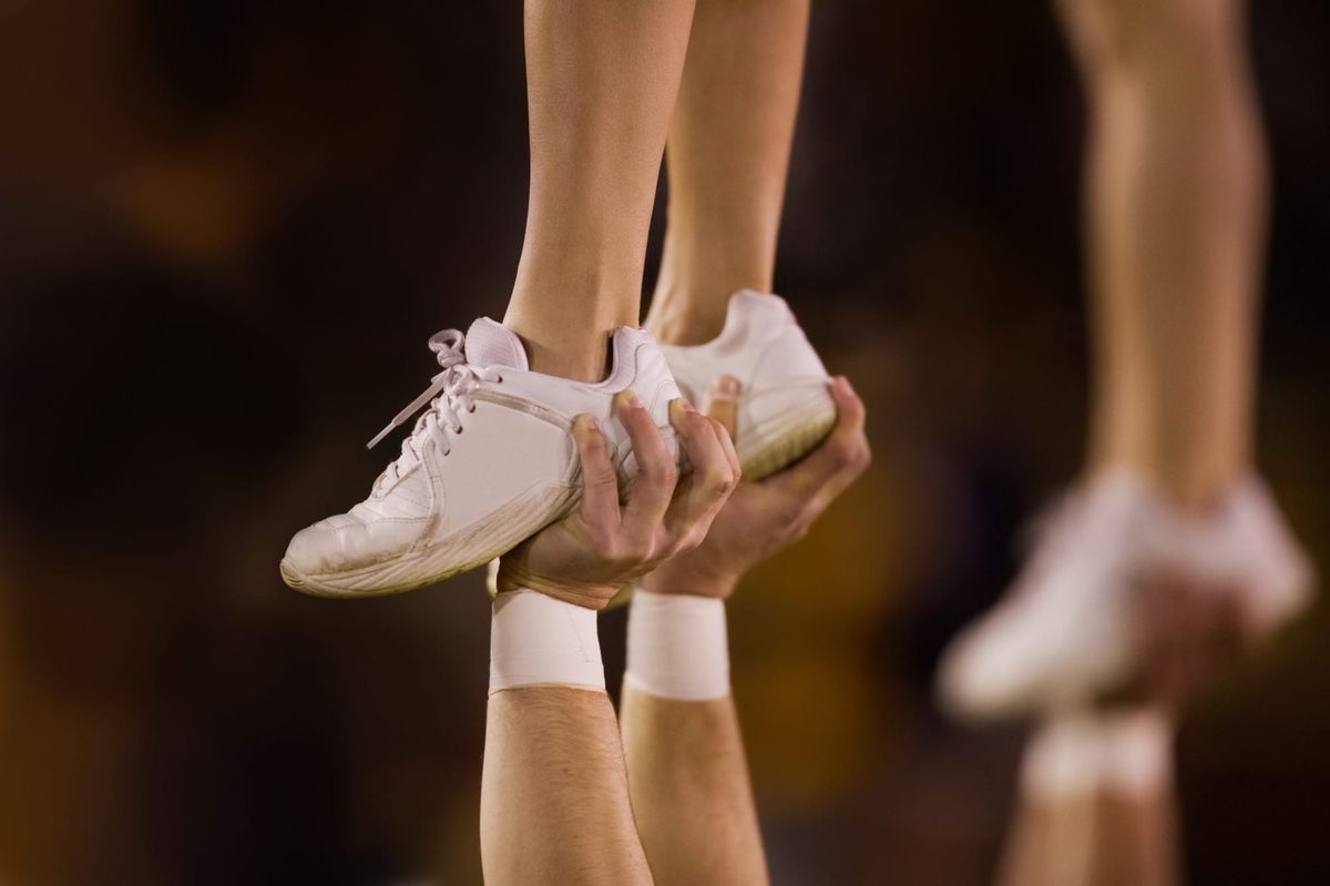 A close-up of hands holding feet up in the air during a cheer competition