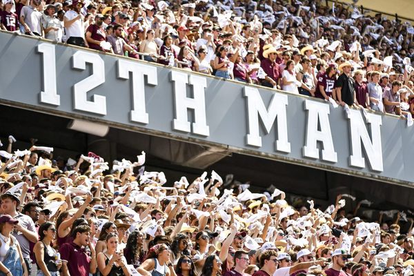 Texas A&M fans cheering with towels in their hands under a sign
