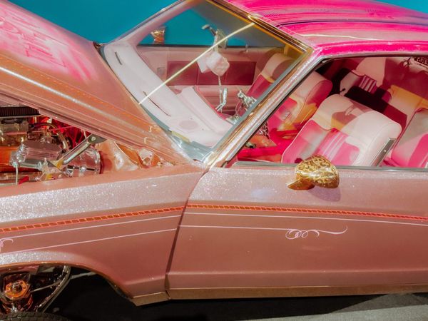 A glittering pink lowrider with the hook popped and dice hanging from the rearview mirror