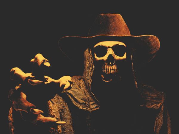 a skeleton or the grim reaper wearing a cowboy hat over dark background