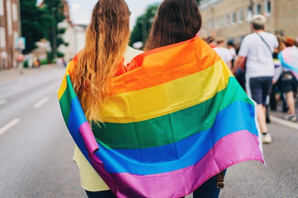 A pride flag wrapped around the arms of two people at a LGBTQ+ pride parade