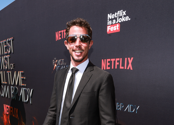 comedian wearing sunglasses standing in front of a netflix backdrop