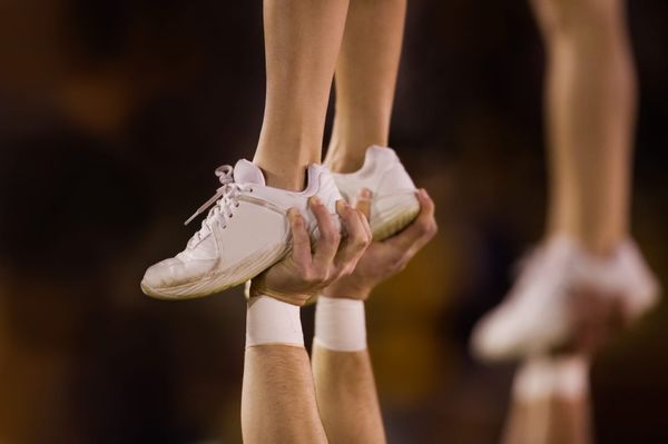 A close-up of hands holding feet up in the air during a cheer competition