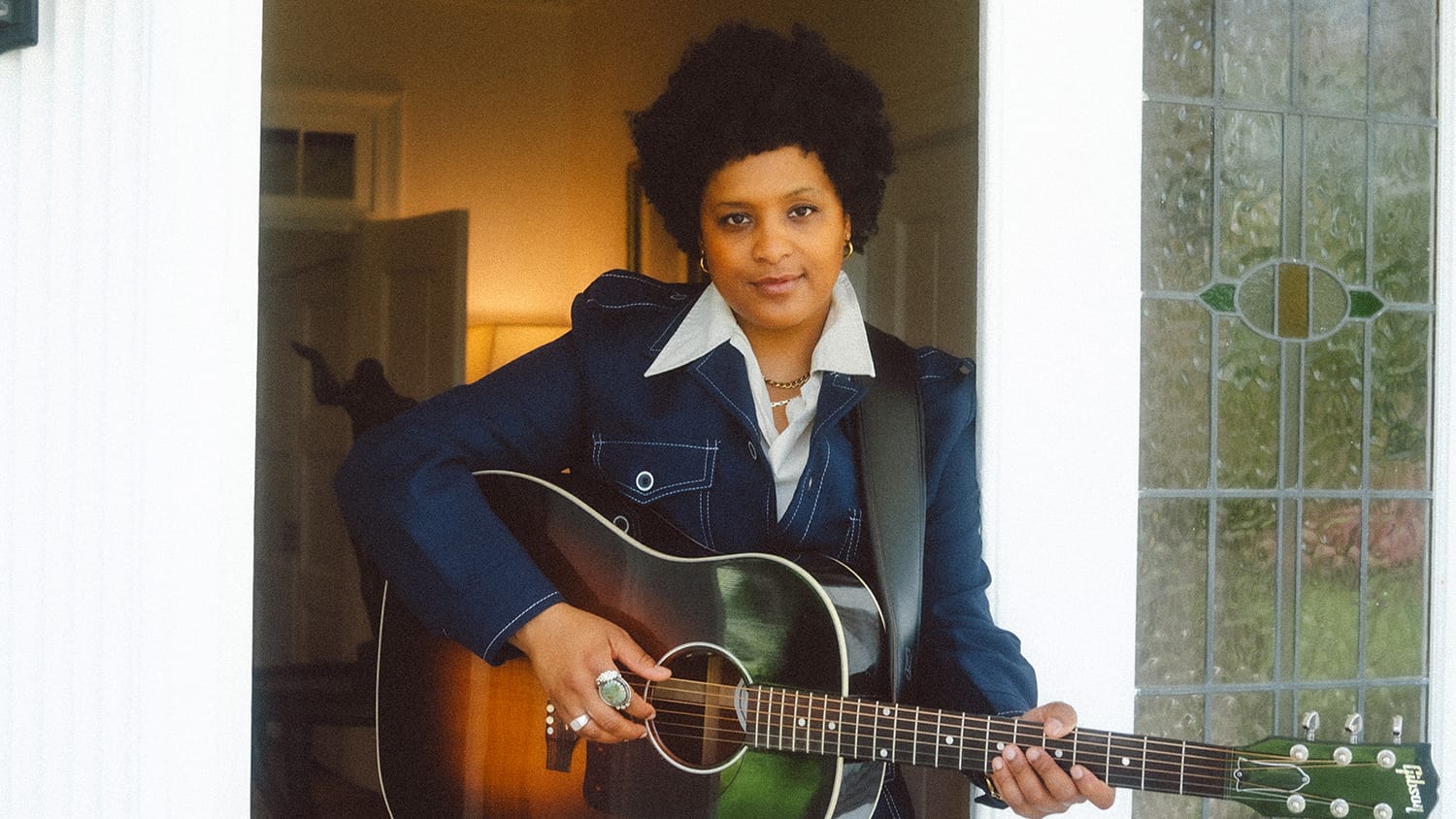 Denitia stands in a doorway holding a guitar