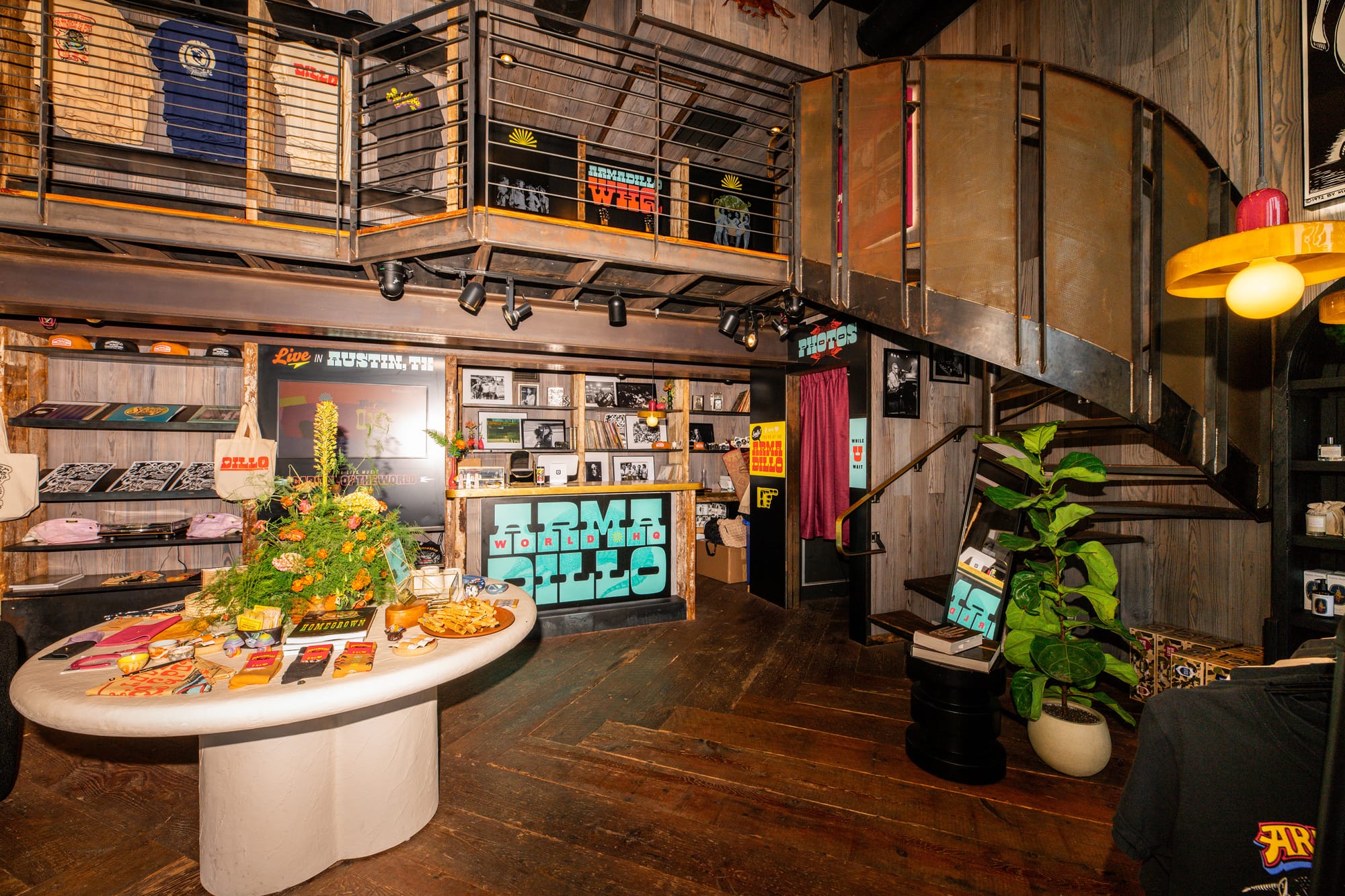 hardwood floors, a white table in the center of the room with merch on it, and an iron staircase inside the armadillo world pop-up