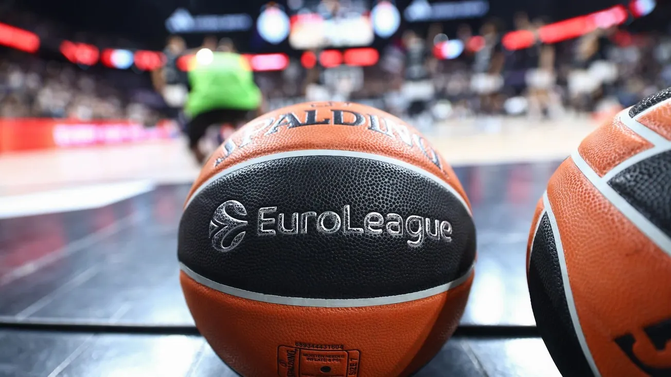 Ballon officiel Spalding de l'Euroleague posé au bord du terrain avant un match, des joueurs à l'échauffement en arrière-plan