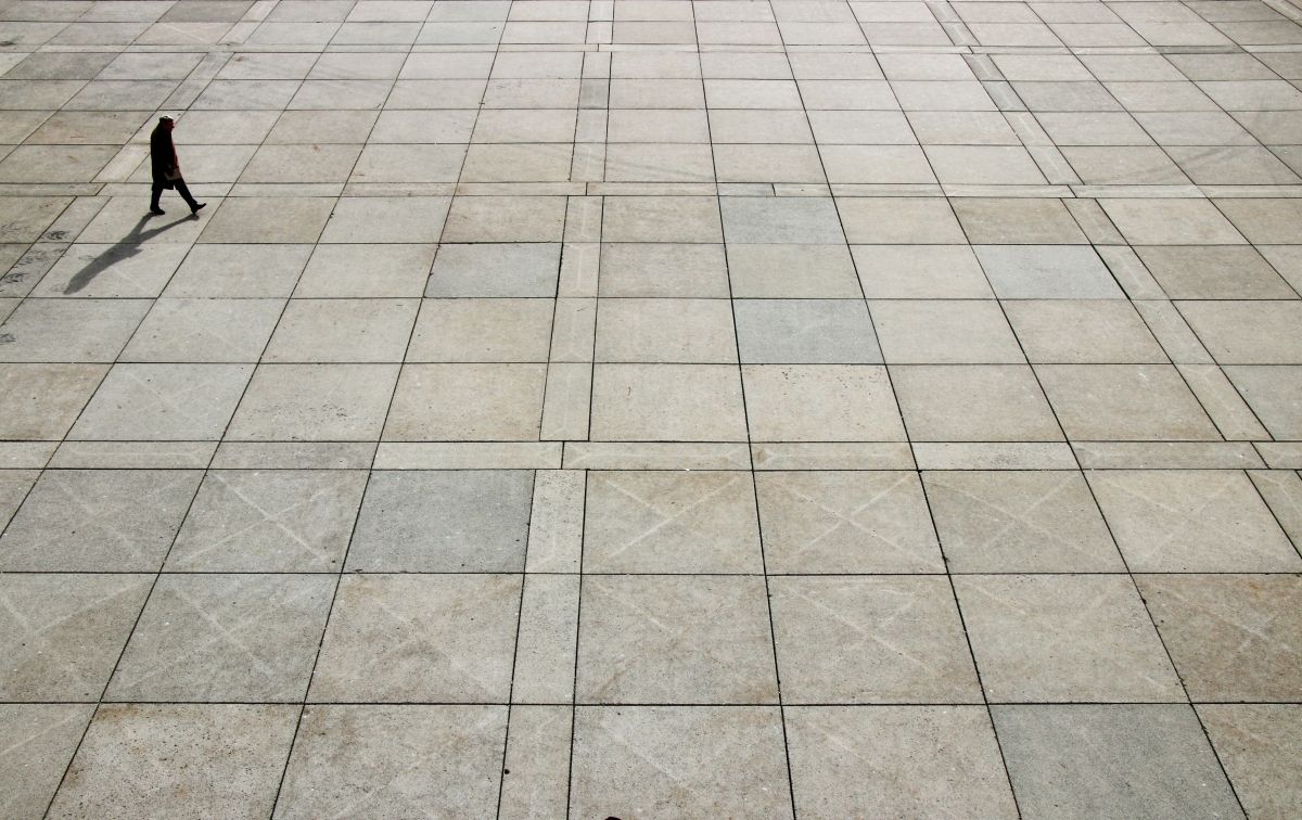 A man in an overcoat works across a floor with square tiles.