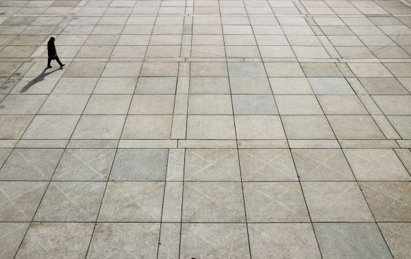 A man in an overcoat works across a floor with square tiles.