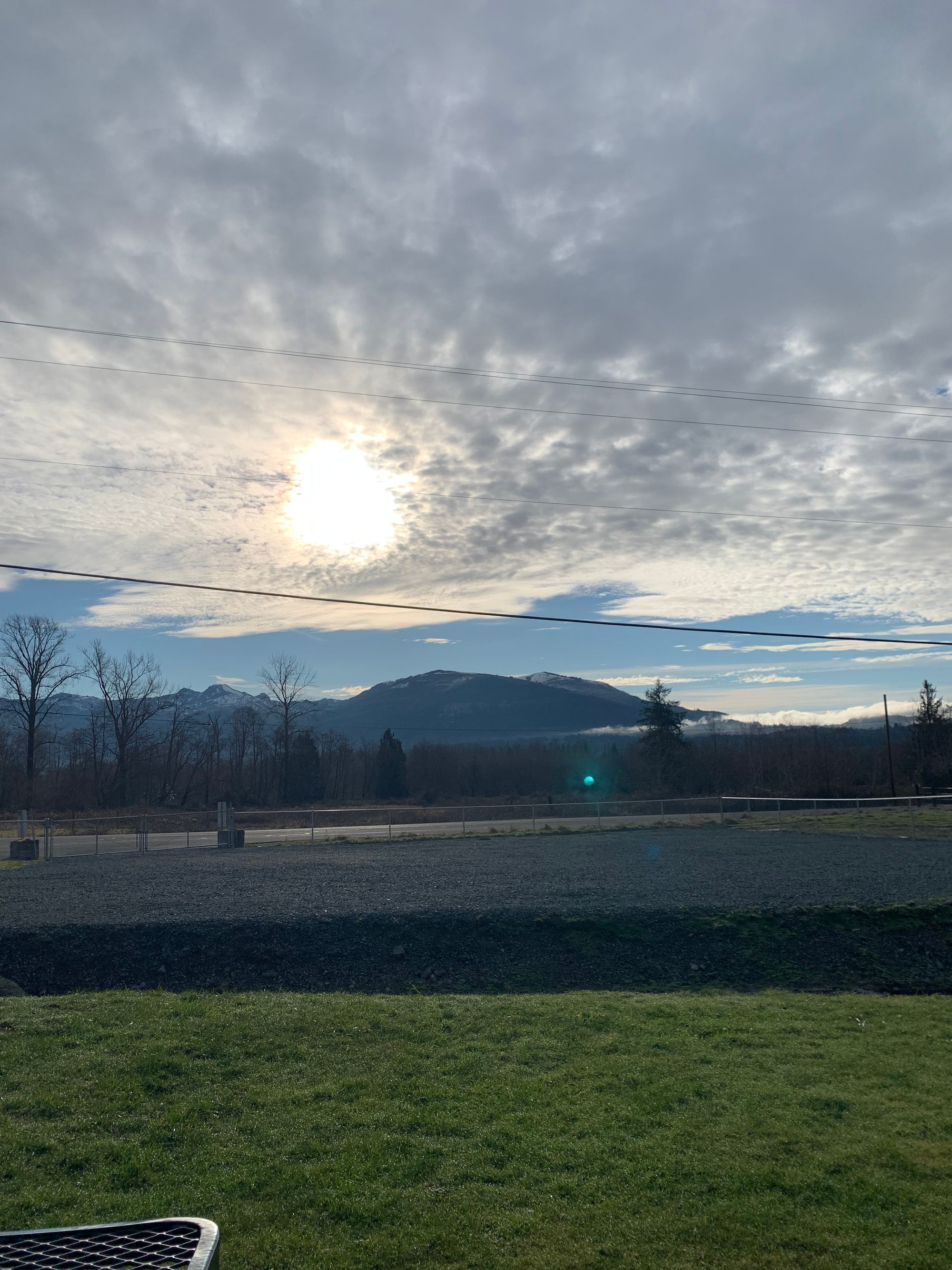 sun breaking through clouds, mountains with snow on them, ditch, green grass