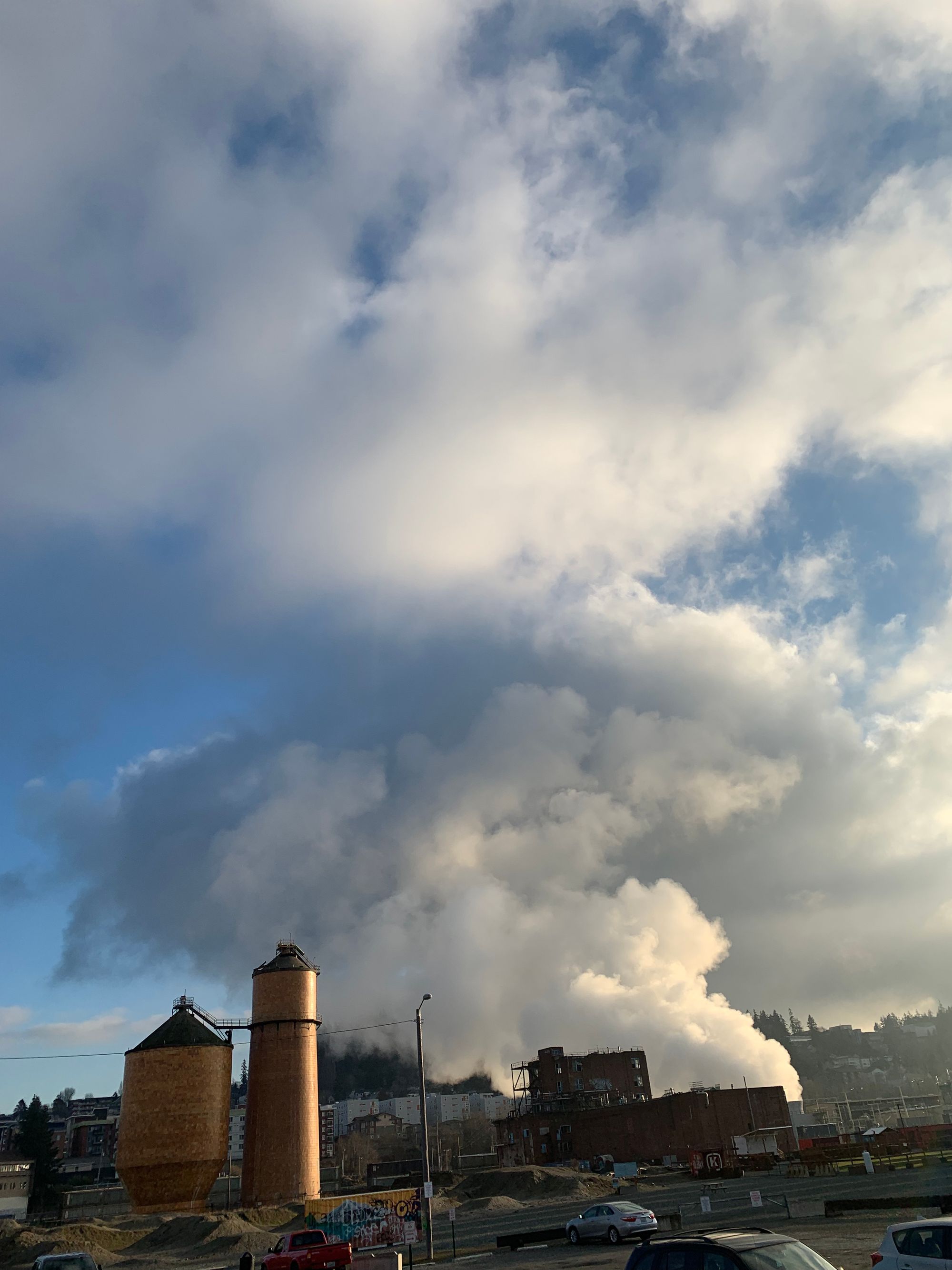 steam rising above abandoned industrial zone with wood and brick buildings, blue sky beyond