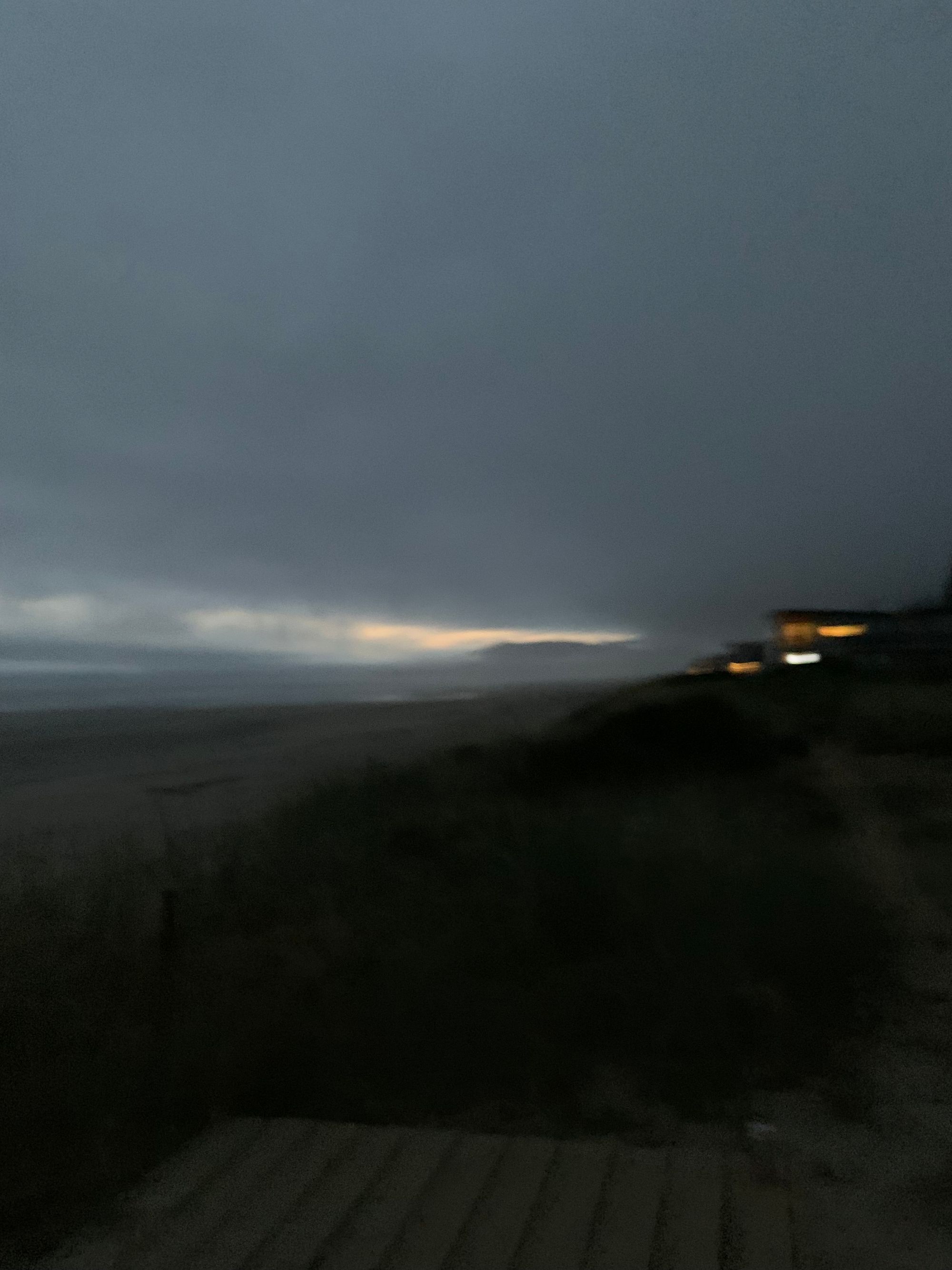 blurry picture of sandy beach & distant lit up houses at night