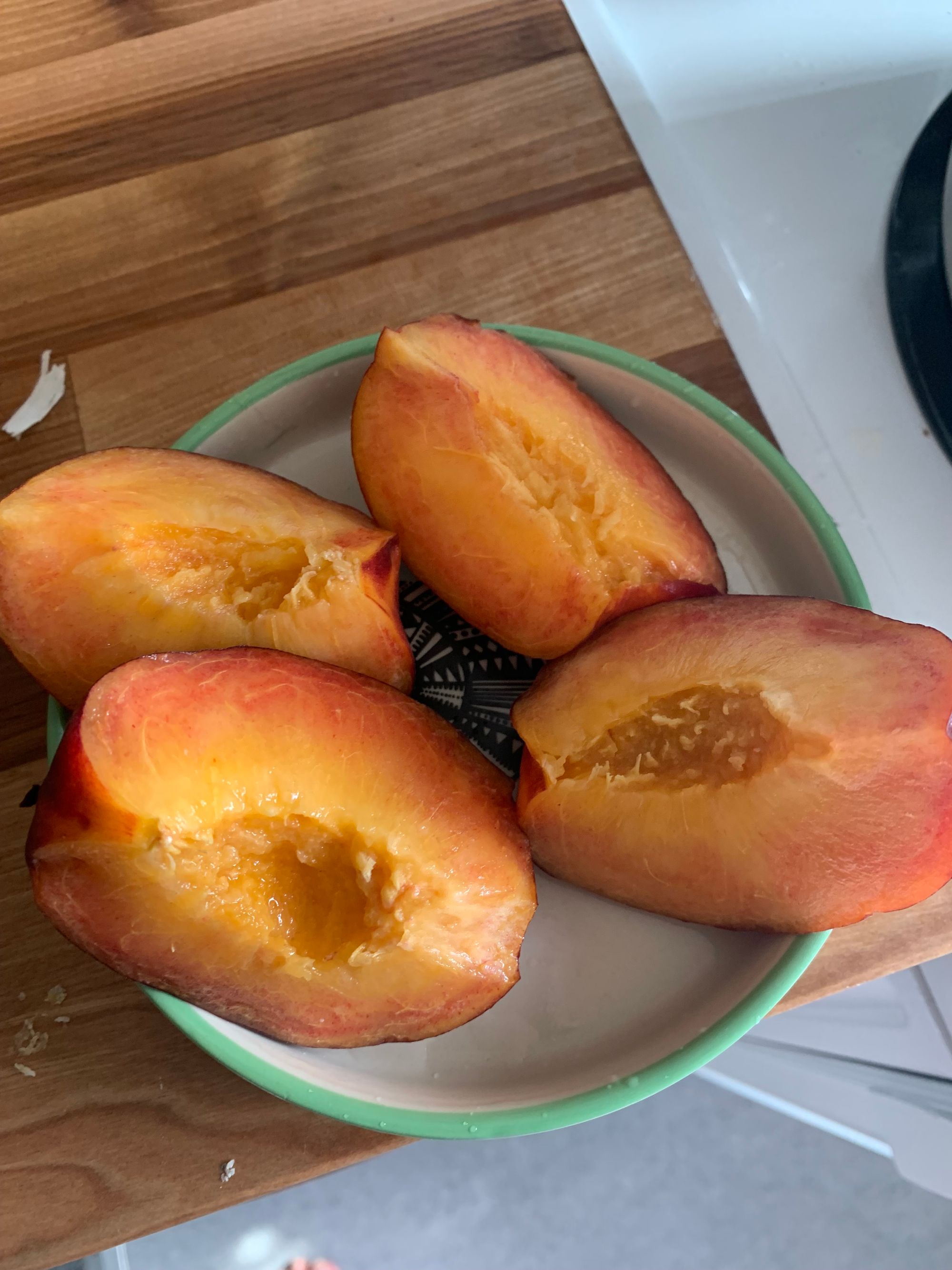 a peach sliced into four pieces on a little green & white plate
