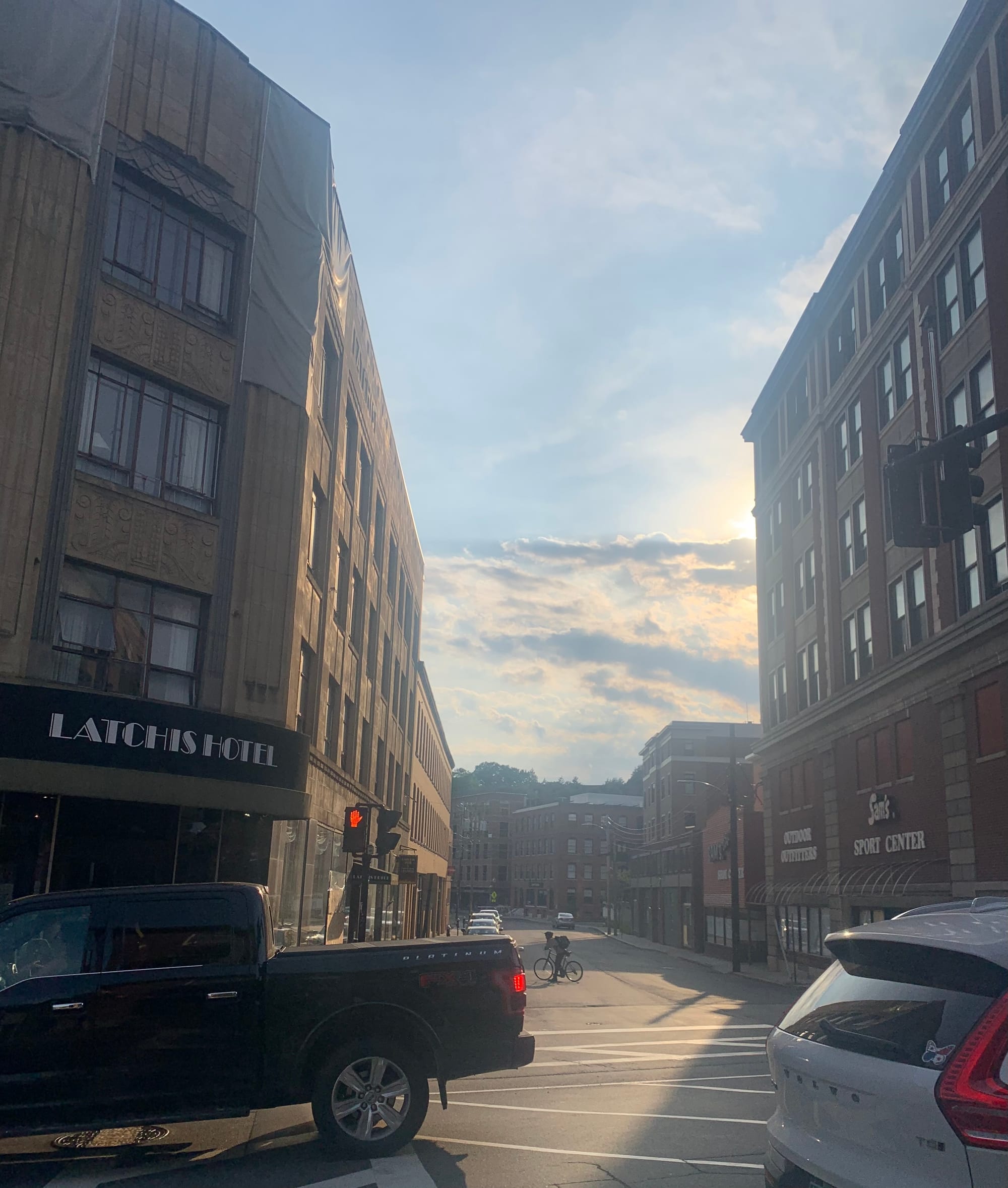 Latchis Hotel on the left, Sam's Sport Center on the right, both tall brick buildings, an alleyway stretching out beyond, a truck, a car & a bicyclist in the intersection