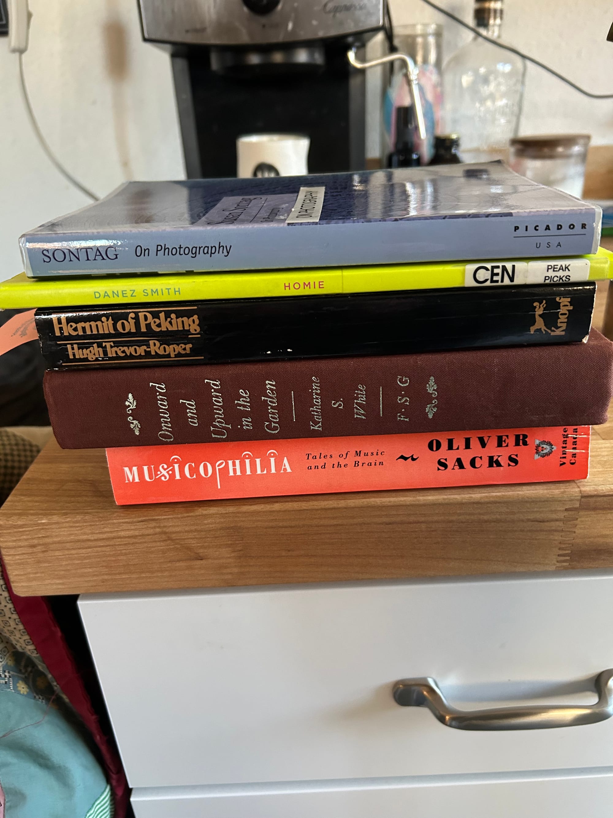stack of used books on a butcher block counter: Musicophilia by Oliver Sacks, Onwards & Upwards in the Garden by Katharine White, Hermit of Peking by Hugh Trevor-Roper, Homie by Danez Smith, On Photography by Susan Sontag