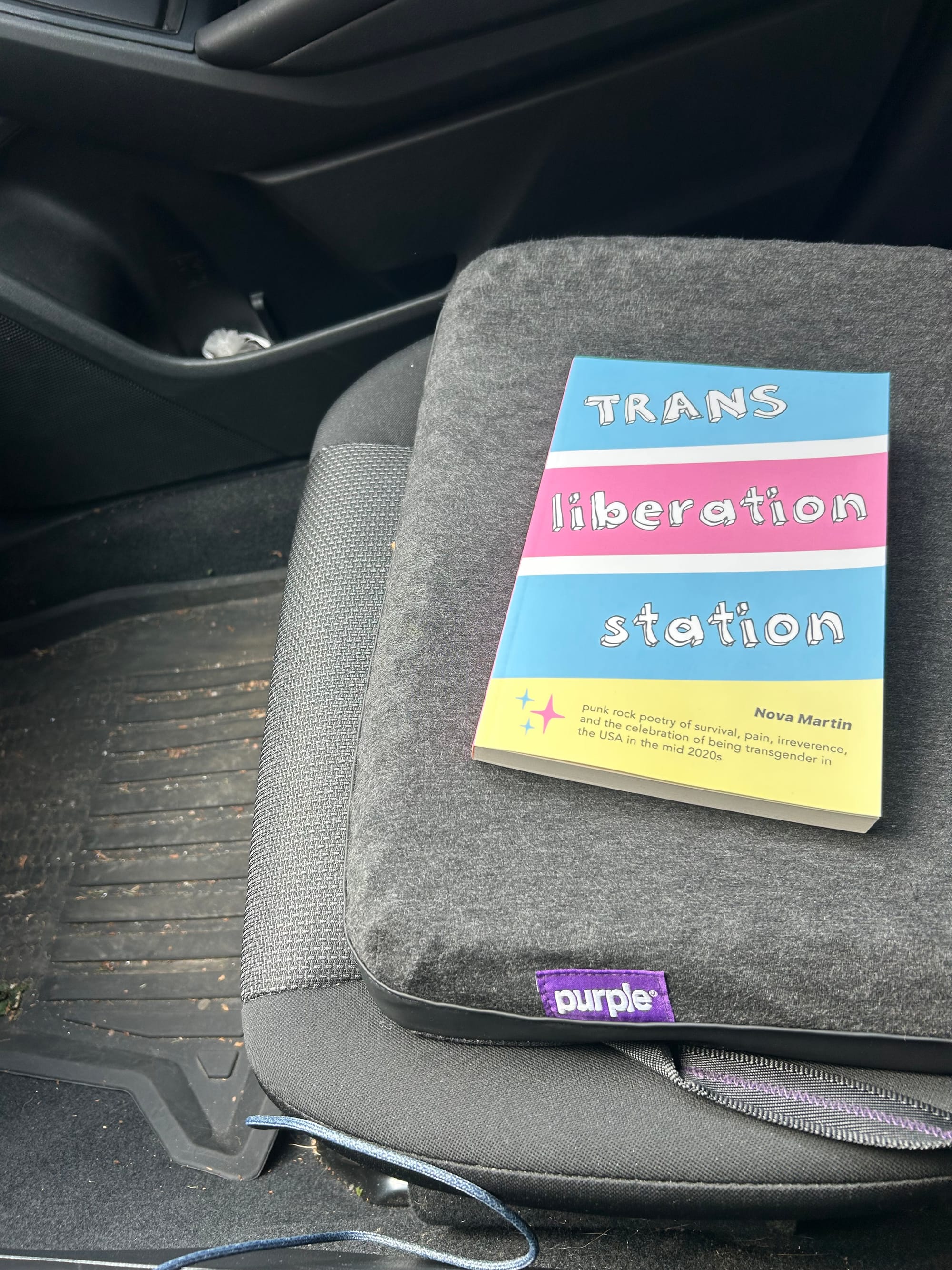 a copy of Nova Martin's book Trans Liberation Station on a black cushion on a black car seat