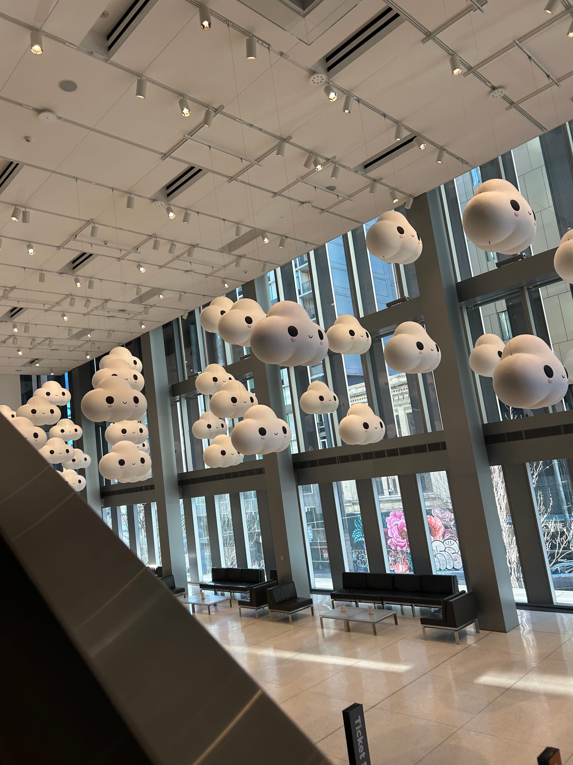 a view of the Seattle Art Museum's lobby from the escalator, an installation of large cartoonish cloud figures hanging from the high ceiling
