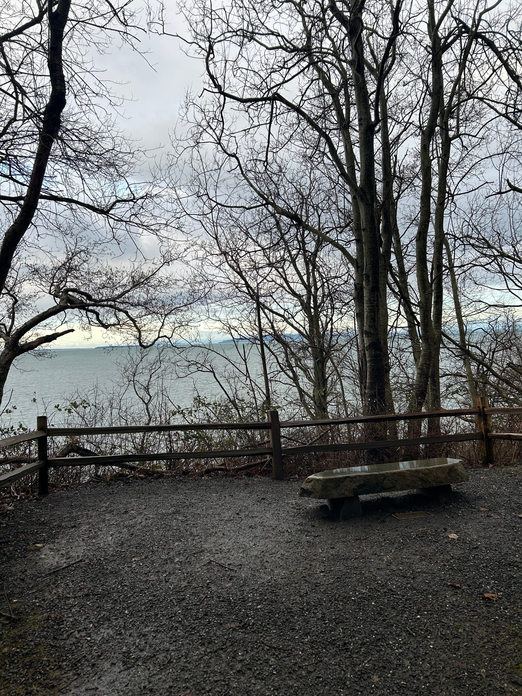 stone bench looking over low wooden fence to a view of a bay, islands in the distance