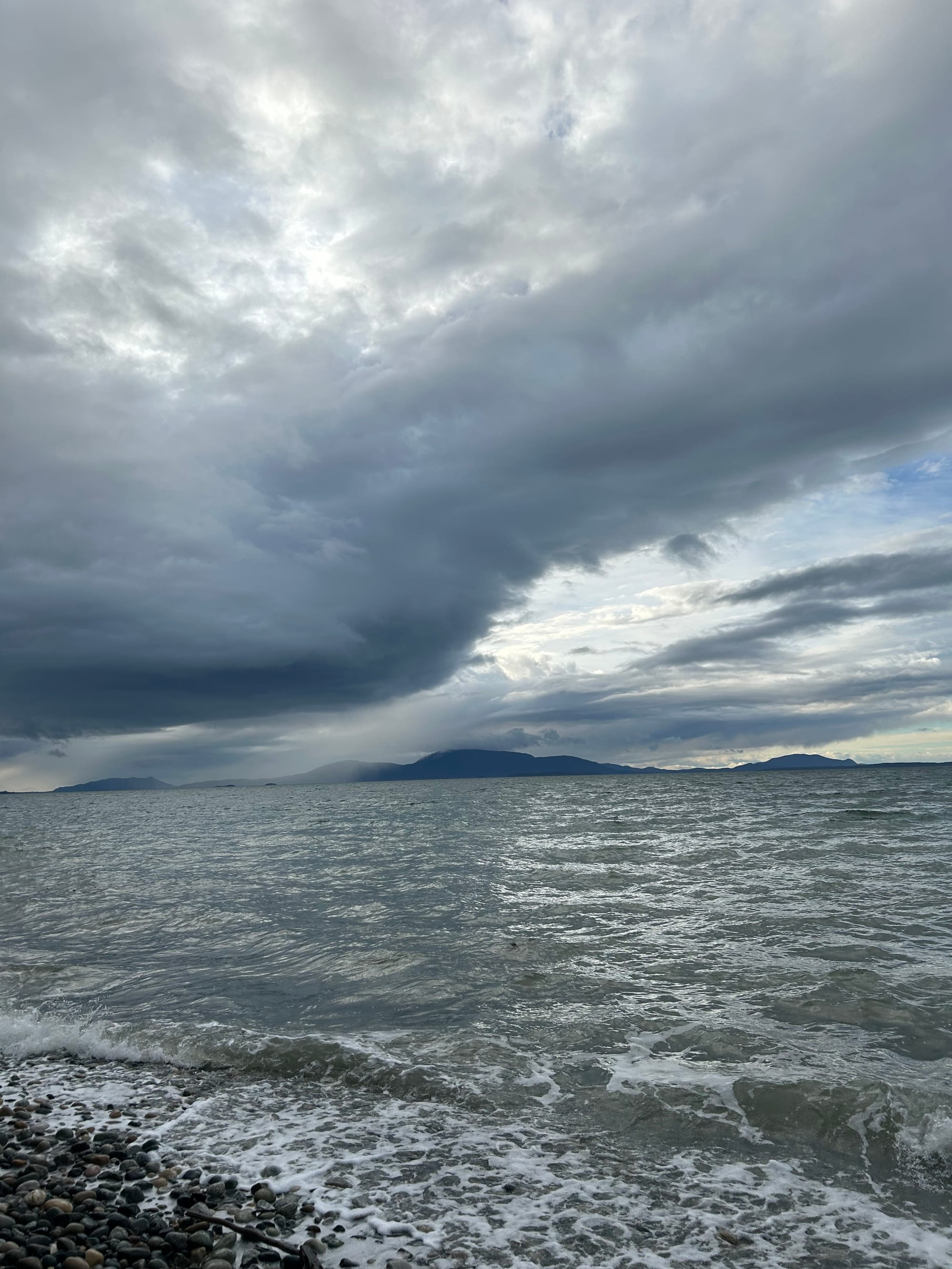 rocky beach, bay waters, islands in the distance, low grey clouds with a streak of distant blue