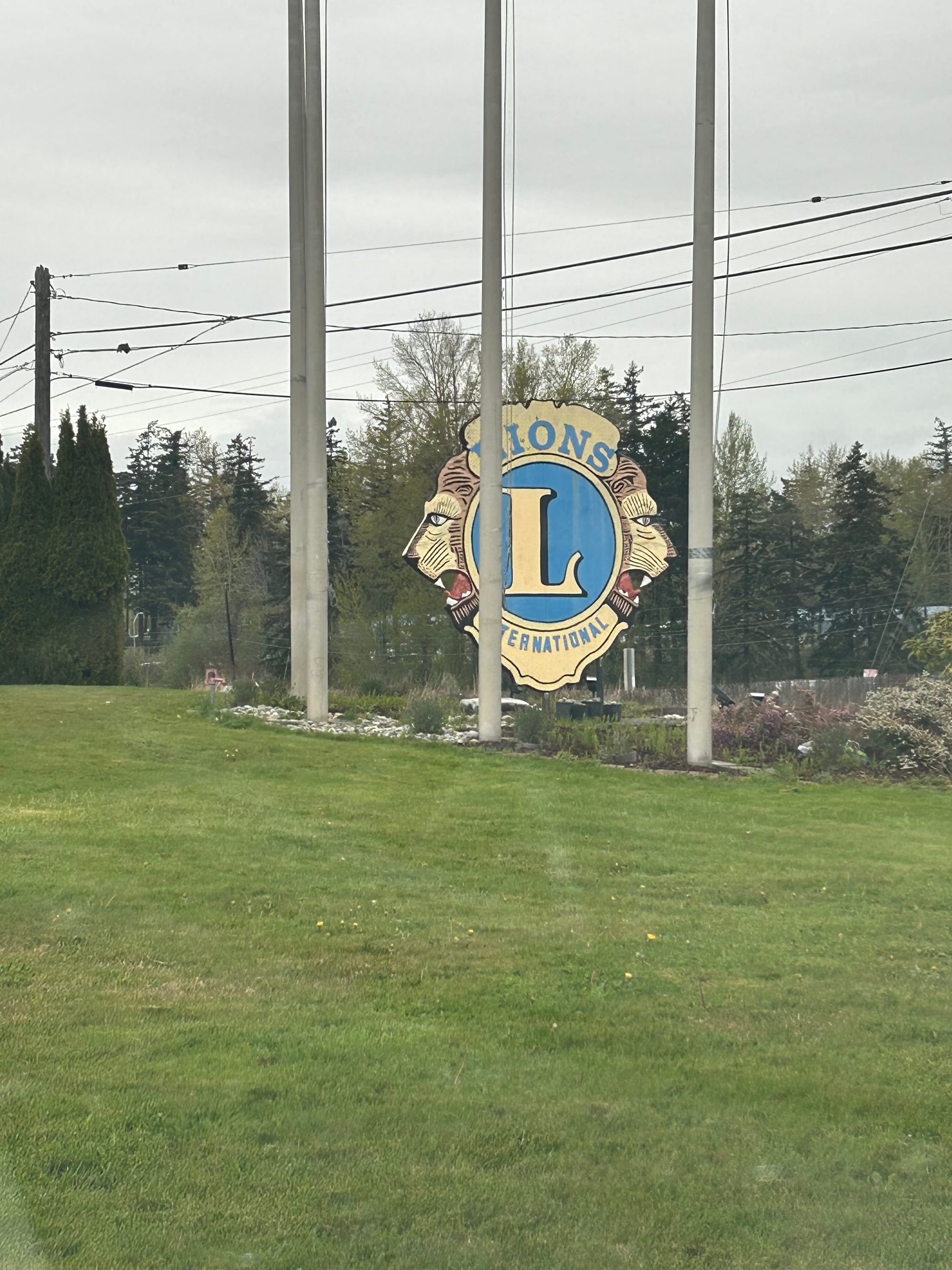 green lawn, light poles, and a large wooden sign for Lions International with two lions' heads facing outward, mid-roar