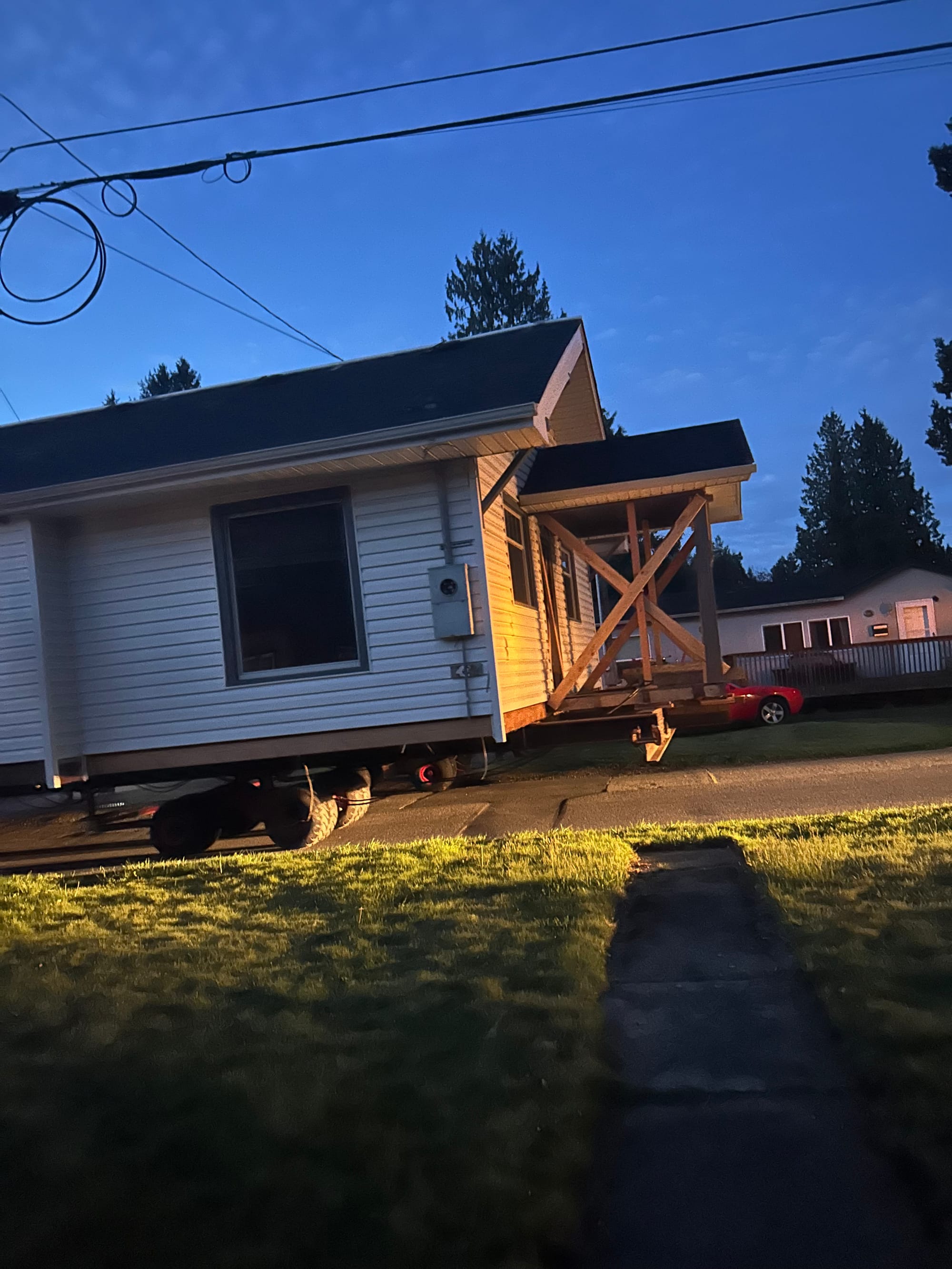 small while house up on a trailer being moved down a street in the pre-dawn light