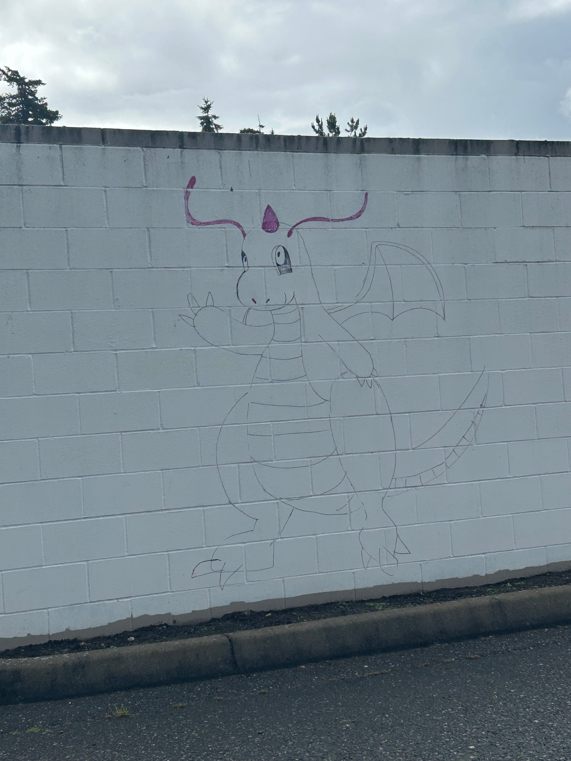graffiti on a white wall of a friendly looking cartoon dragon creature