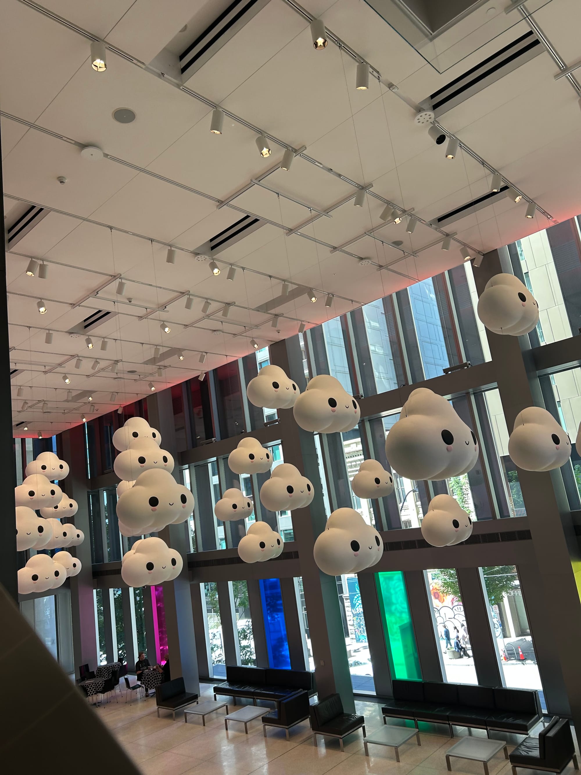 a view from the escalator of Seattle Art Museum's lobby, installation of large white smiling clouds hung from the ceiling