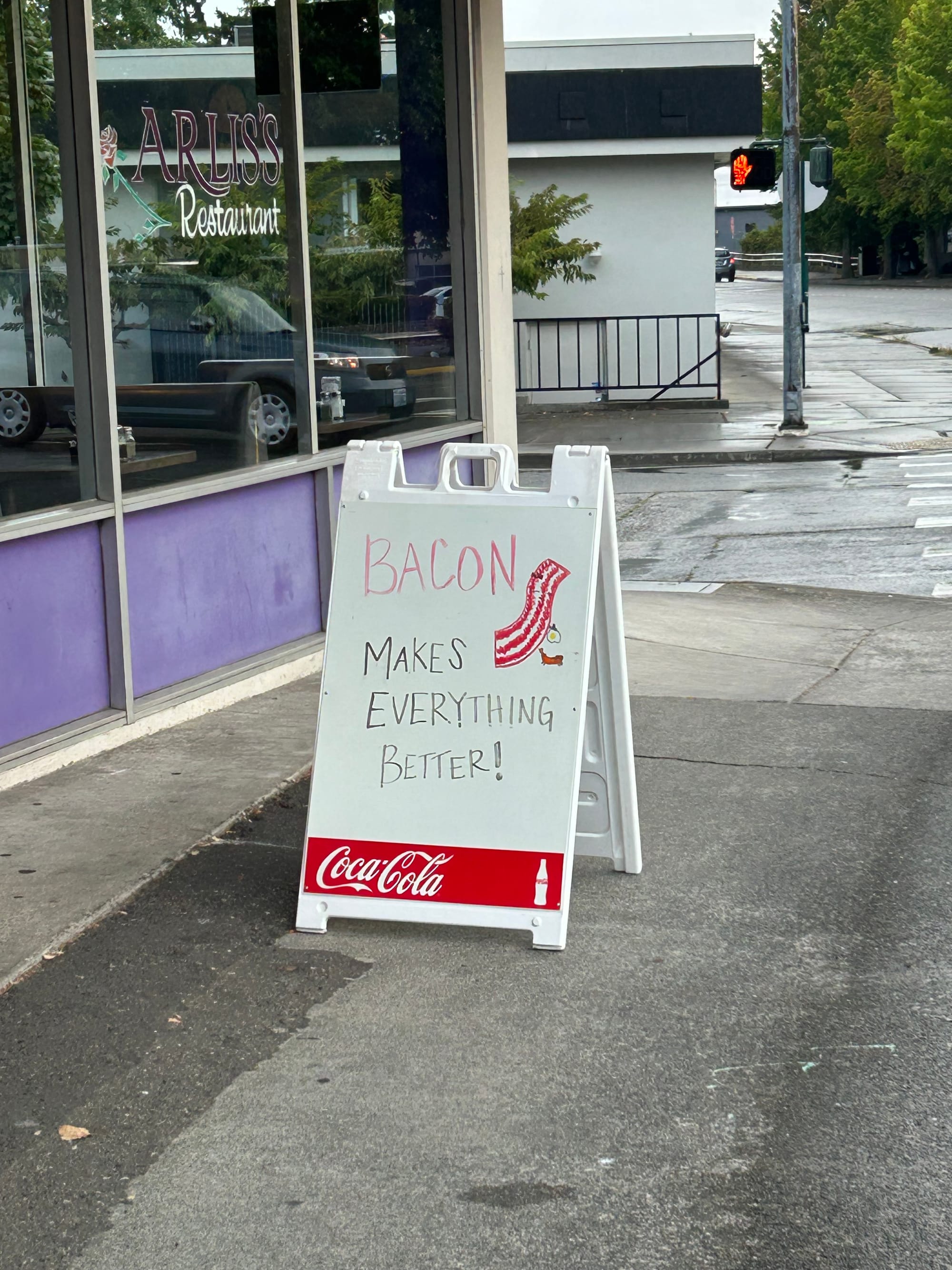 Standing sign outside a diner reading "Bacon makes everything better!"