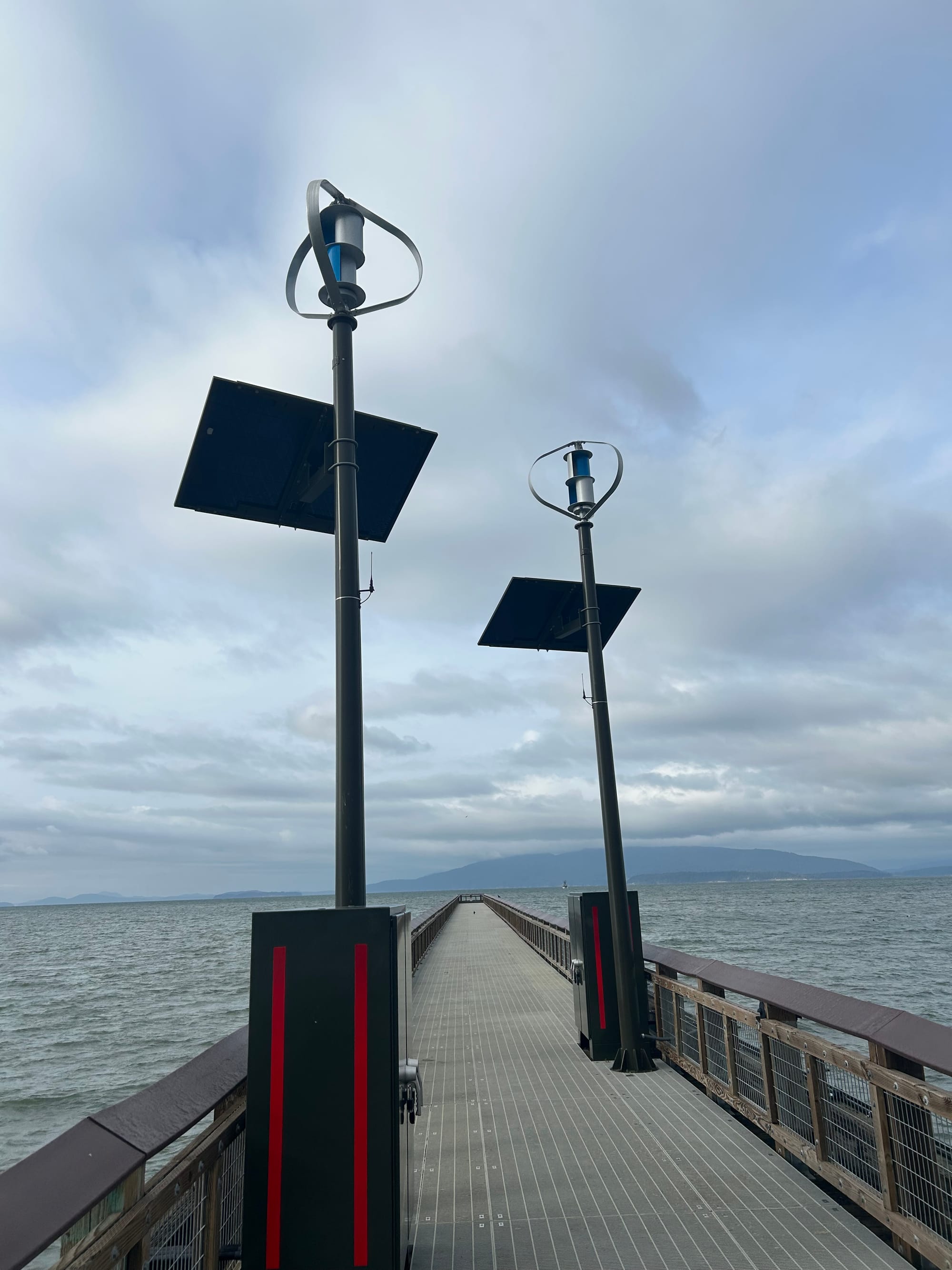 long pier extending out into Bellingham Bay with two large metal lockers and solar lights extending upward. grey water, grey cloudy skies.