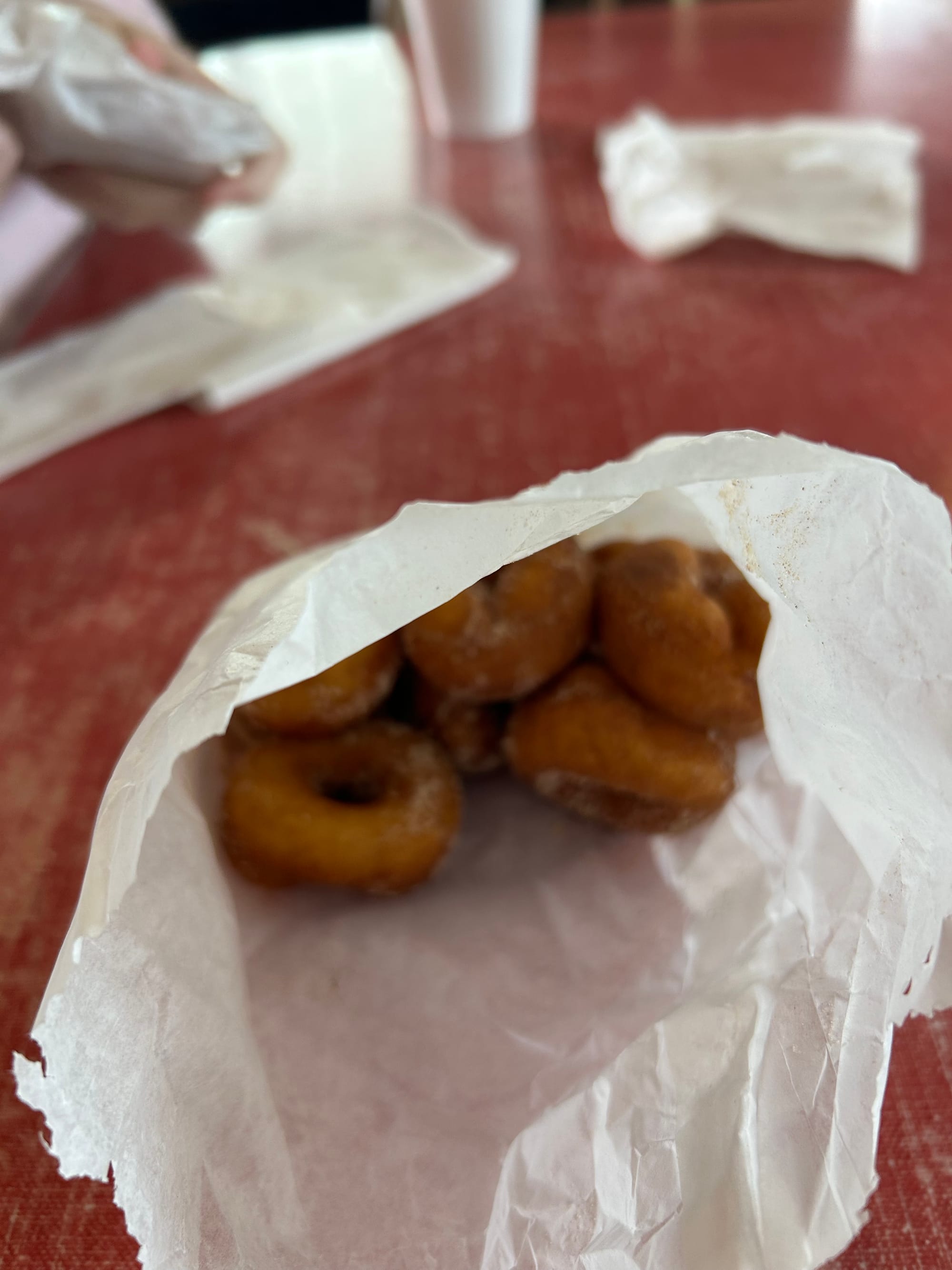 white paper bag with little fresh apple cider donuts sitting on a wooden table.
