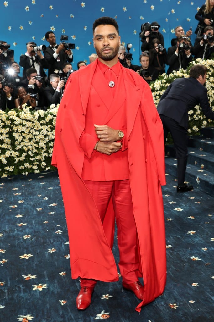 Regé-Jean Page posing in a bright red suit with a long matching red coat.