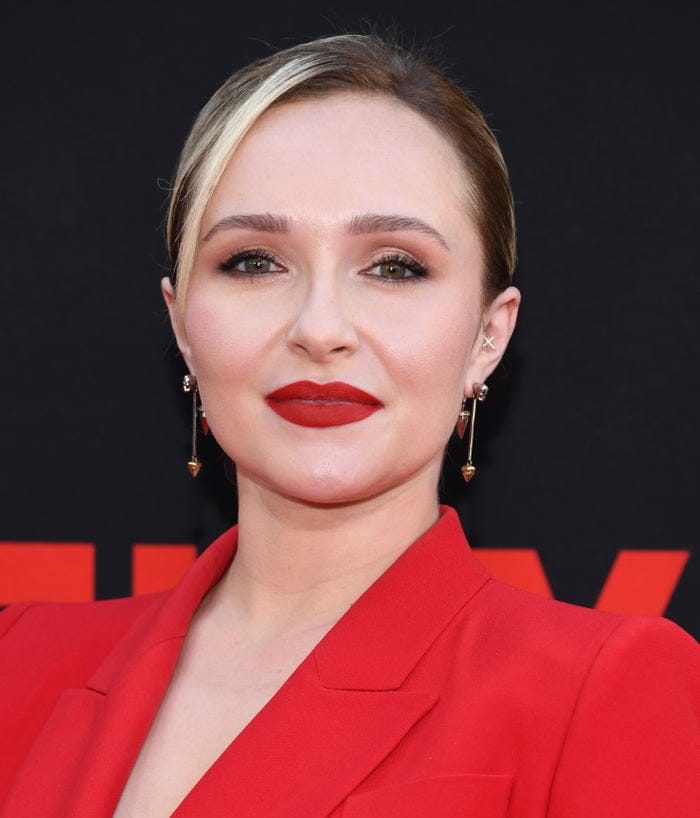 Person with elegant updo and striking red lipstick wears a tailored jacket and dangling earrings