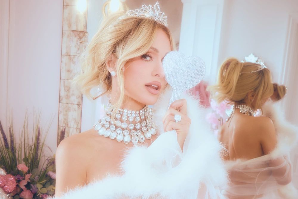 A screenshot or repost of Paris Hilton's actual Instagram bathtub photo showing her covered in soap bubbles with visible Parivie Beauty branding. The image should capture the polished, asp...