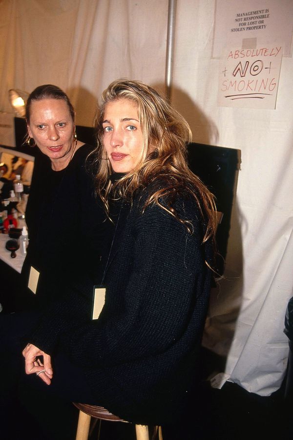Archival photograph of Carolyn Bessette-Kennedy in minimalist black outfit, photographed by paparazzi while walking, face turned away from camera or expression neutral/guarded — capturing ...