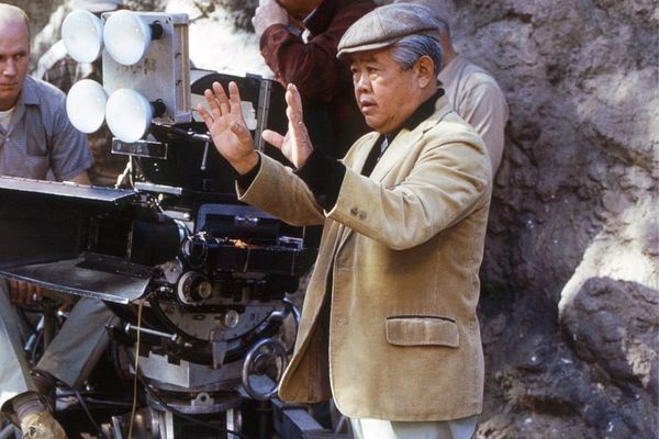 Archival black-and-white photograph of James Wong Howe on set with a camera, ideally from the 1940s-1960s, showing him at work behind the lens—the image should convey his technical mastery...