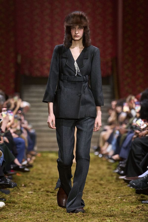 A runway look from Miu Miu Fall 2026 that clearly demonstrates the collection's referential, ironic aesthetic — ideally a look combining preppy codes (pleated skirt, blazer, knee socks) wi...